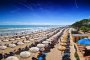 Lunga spiaggia con ombrelloni e persone in mare.