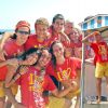 Gruppo di giovani felici in magliette rosse sulla spiaggia, vicino al mare.