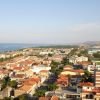 Vista panoramica di un'area costiera con case dai tetti rossi e il mare sullo sfondo.