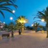 Viale pedonale di sera con palme e lampioni accesi.