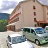 Edificio rosa con parcheggio, montagne verdi.