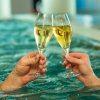 Mani che brindano con bicchieri di spumante in piscina.